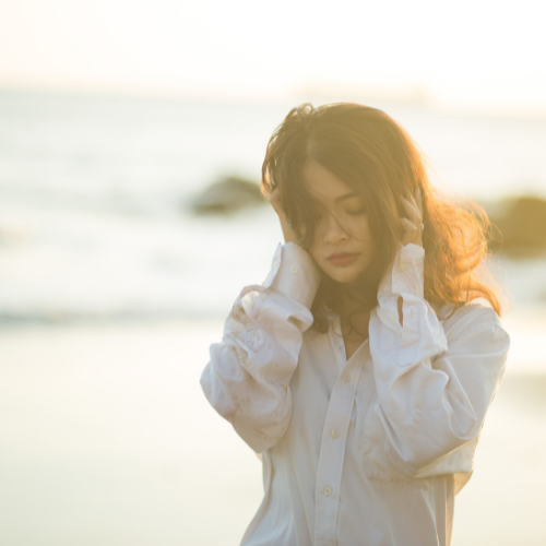 海辺で耳を塞ぐ女性の写真